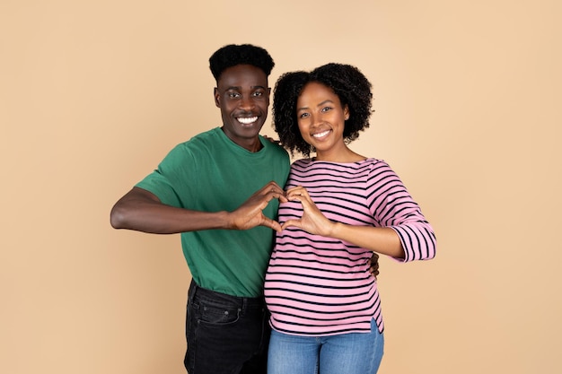 Una alegre joven negra con una gran barriga disfruta del embarazo y espera un bebé que hace un gesto de corazón