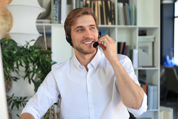 Alegre joven operador de teléfono de soporte en auriculares en el lugar de trabajo mientras usa la computadora