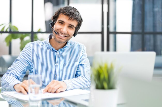 Alegre joven operador de teléfono de soporte en auriculares en el lugar de trabajo mientras usa el servicio de ayuda informática y el concepto de centro de llamadas de consultoría de clientes