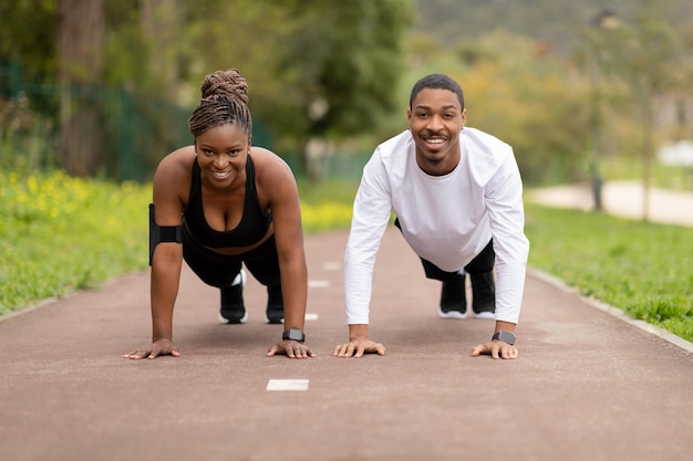 Alegre joven pareja afroamericana haciendo ejercicio push up en el parque al aire libre disfruta del entrenamiento en