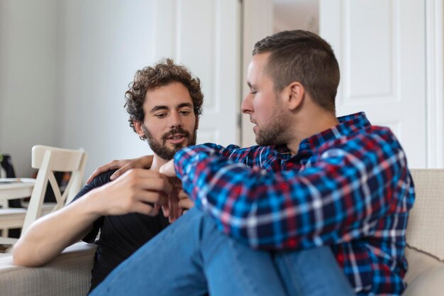 Alegre joven pareja gay sentados juntos Dos afectuosos amantes masculinos sonriendo alegremente mientras se abrazan