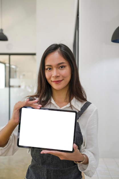 Alegre joven propietaria mostrando tableta digital mientras está de pie en la cafetería
