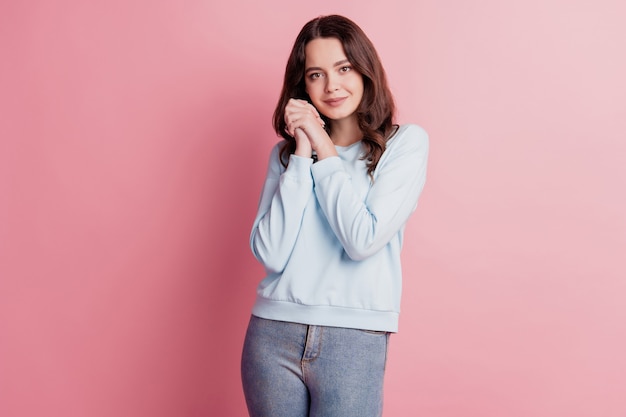 Alegre joven relajada posando manos mejilla aislada sobre fondo rosa