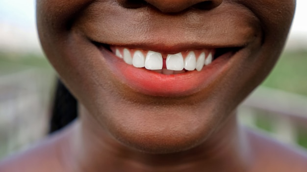 Alegre joven rostro de mujer afroamericana con lápiz labial rojo brillante sonríe contra el fondo borroso extreme close view