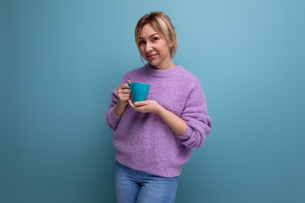 Alegre joven rubia milenaria en un look casual con una taza de café en un fondo brillante