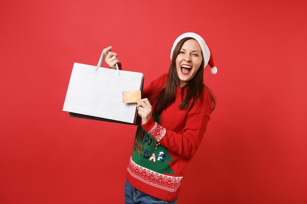 Alegre joven Santa con tarjeta de crédito, bolsas de paquetes con compras después de ir de compras aisladas sobre fondo rojo brillante. Feliz año nuevo 2019 celebración concepto de fiesta navideña. Simulacros de espacio de copia.