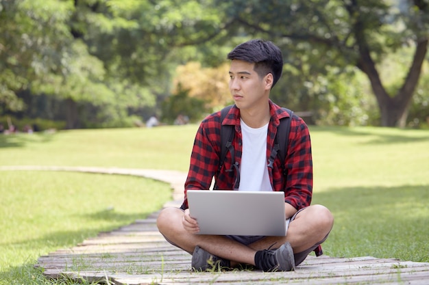 Alegre joven sentado en el parque y usando una computadora portátil