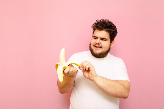 Alegre joven con sobrepeso sostiene un plátano en su mano Concepto de dieta