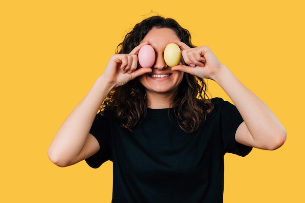 Alegre joven sonriente cubre sus ojos con huevos de Pascua de colores