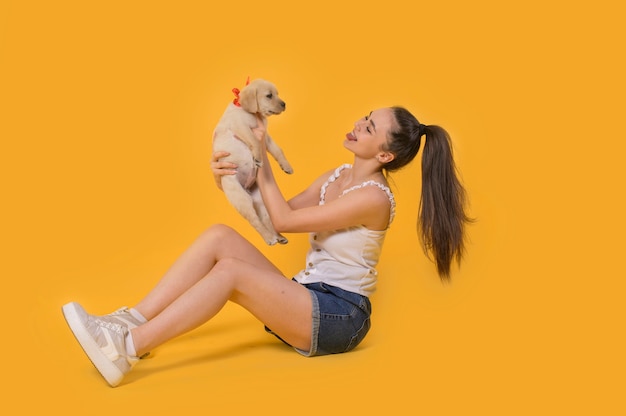 Alegre joven sosteniendo su cachorro riendo Retrato interior de niña sonriente posando con cachorro