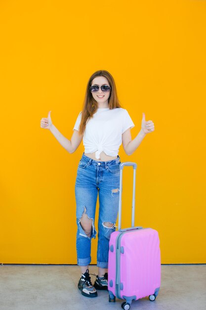 alegre joven vestida con ropa de verano y gafas de sol de pie con una maleta