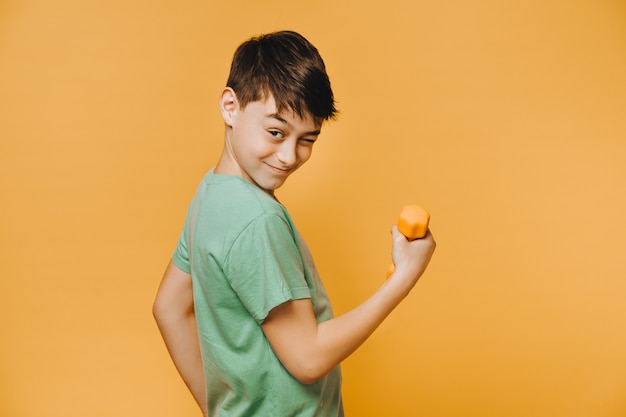 Alegre joven vestido con una camiseta verde, guiños y haciendo ejercicio con pesas para mejorar su estado físico Concepto de personas activas y optimistas.