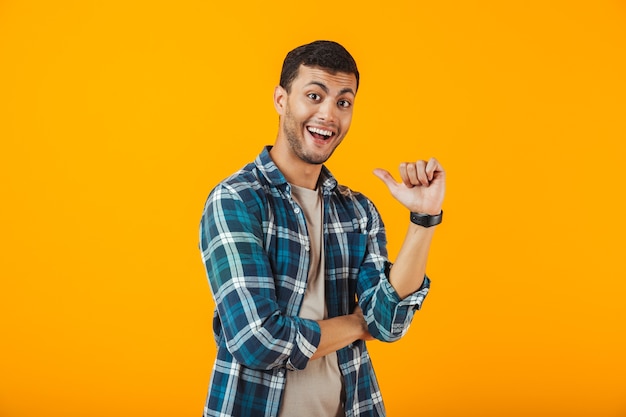 Alegre joven vistiendo camisa a cuadros se encuentran aisladas sobre pared naranja, señalando con el dedo a sí mismo