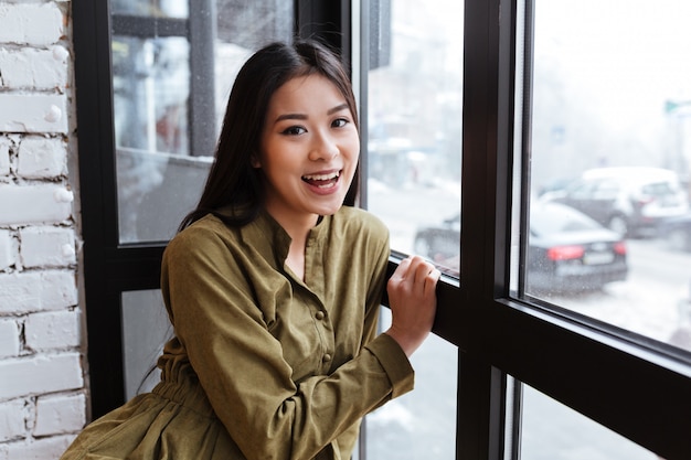 Alegre jovencita asiática sentada en el café junto a la ventana