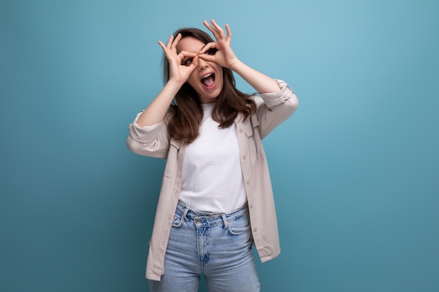 Alegre jovencita de pelo oscuro feliz con ropa informal haciendo muecas con fondo azul