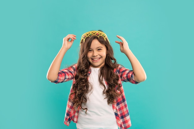 Alegre jovencita con pelo rizado use corona sobre fondo azul, arrogancia