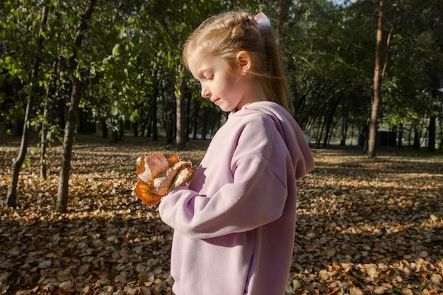 Alegre jovencita rubia feliz con un ramo de hojas de otoño posa en el parque