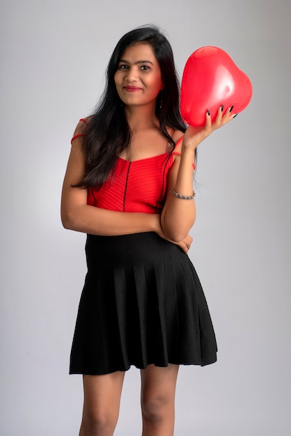 Alegre linda chica en elegante traje rojo y negro posando con globo en forma de corazón.