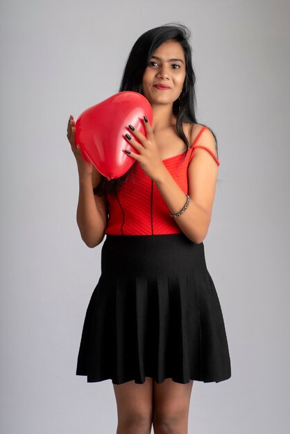 Alegre linda chica en elegante traje rojo y negro posando con globo en forma de corazón.