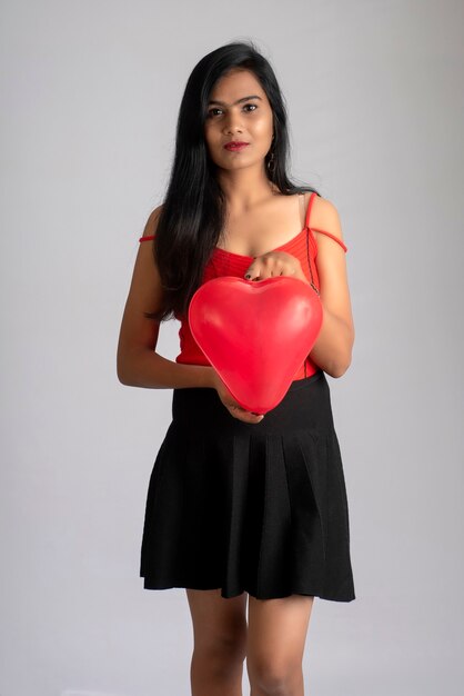 Alegre linda chica en elegante traje rojo y negro posando con globo en forma de corazón.