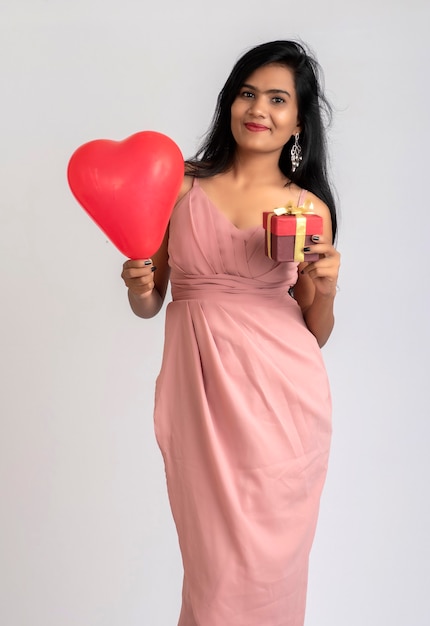 Alegre linda garota com roupa chique, posando com balão em forma de coração e caixa de presente.