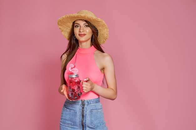 Alegre linda garota da praia com chapéu de verão, posando de maiô corporal com coquetel na mão