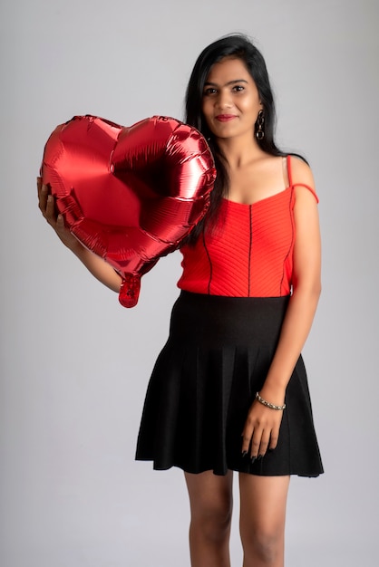 Alegre linda garota vestida de vermelho e preto chique, posando com balão em forma de coração.