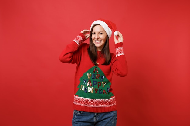 Alegre linda jovem santa no suéter tricotado de mãos dadas no chapéu de natal, isolado no fundo da parede vermelha brilhante. conceito de festa de feriado de celebração de ano novo feliz 2019. simule o espaço da cópia.