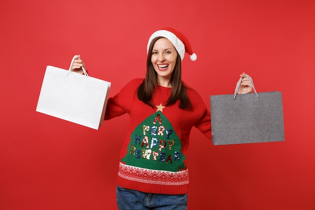 Alegre linda jovem santa segurando pacotes sacos com as compras depois de fazer compras isoladas no fundo da parede vermelha brilhante. Conceito de festa de feriado de celebração de ano novo feliz 2019. Simule o espaço da cópia.