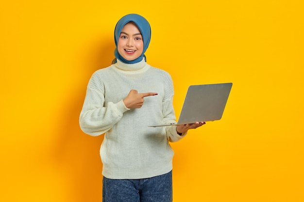 Alegre linda mulher asiática de suéter branco usando laptop recebeu boas notícias em e-mail isolado sobre fundo amarelo pessoas conceito de estilo de vida religioso