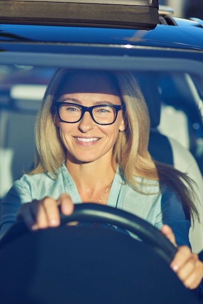 Alegre linda mulher madura ou mulher de negócios usando óculos, dirigindo seu carro moderno