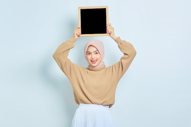 Alegre linda mulher muçulmana asiática em suéter marrom mostrando lousa isolada sobre fundo branco Pessoas conceito de estilo de vida religioso