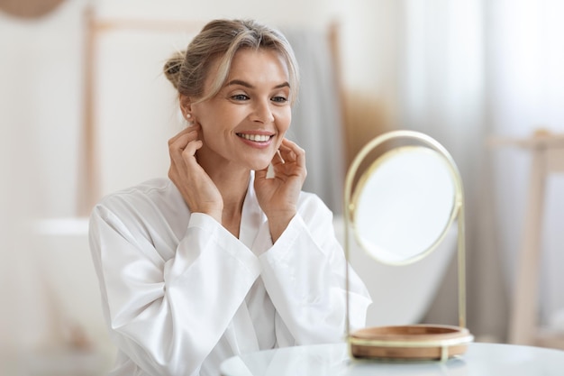 Alegre linda senhora adulta usando creme hidratante para o rosto