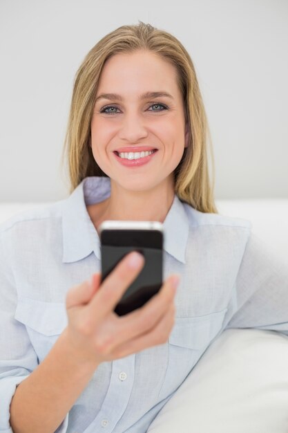 Alegre loiro casual relaxante no sofá segurando o smartphone