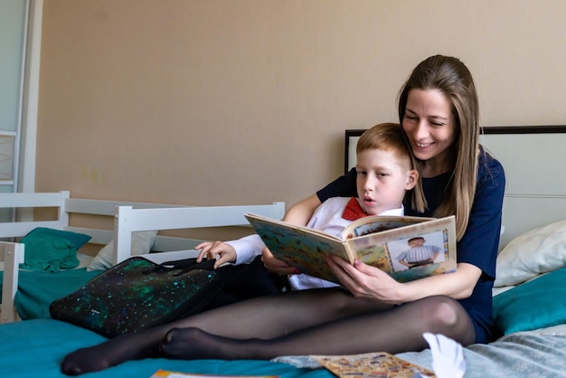 Alegre madre abrazando a su hijo y leyendo una tarjeta de felicitación hecha a mano con el corazón mientras descansa en la cama durante la celebración navideña del día de la madre en casa