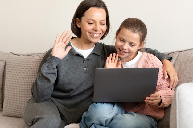 Alegre madre caucásica de mediana edad y su pequeña hija agitan las manos miran el gesto de saludo de la computadora