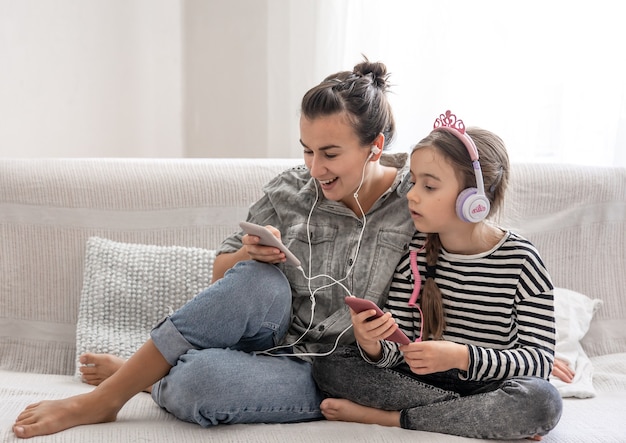 Alegre mãe e filha estão descansando em casa, ouvindo música em fones de ouvido. conceito de uma família feliz e relações amigáveis.