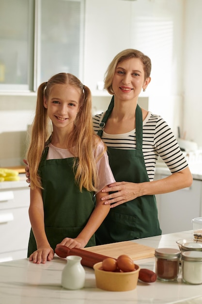 Alegre mãe e filha nos mesmos aventais cozinhando na cozinha