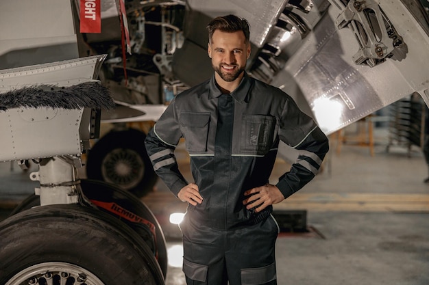 Alegre mecânico masculino em pé perto de avião no hangar