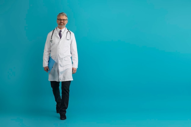 Alegre médico de mediana edad con historial médico caminando en azul