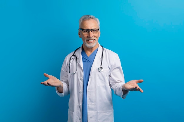 Alegre médico senior gesticulando sobre fondo azul.