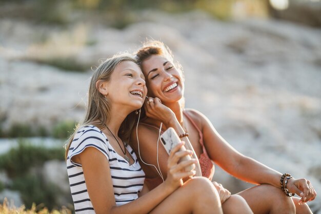 Alegre menina adolescente e sua jovem mãe se divertindo enquanto desfruta de férias de verão em uma praia de rocha do mar.