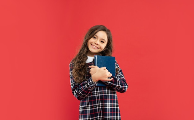 Alegre menina adolescente segurando o livro na infância de fundo vermelho