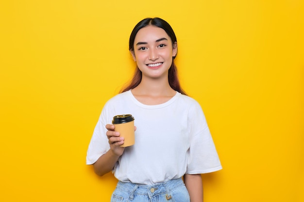 Alegre menina bonita em camiseta branca segurando uma xícara de café isolada em fundo amarelo