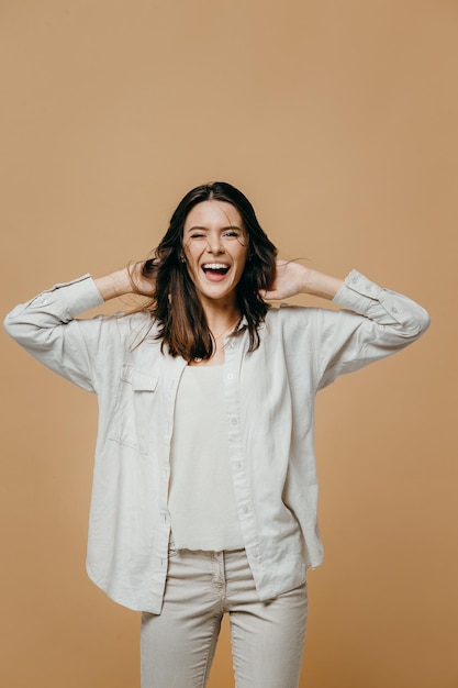 Alegre menina bonita feliz olhando para a câmera sorrindo rindo sobre fundo bege