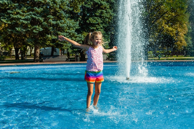 Alegre menina bonitinha está brincando na fonte. a criança está se divertindo em um parque de verão na fonte da cidade.