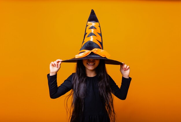 Alegre menina caucasiana com fantasia de bruxa de Halloween isolada em fundo amarelo.