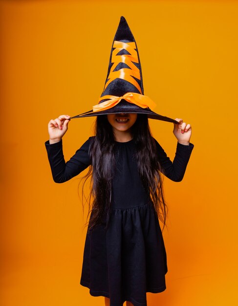 Foto alegre menina caucasiana com fantasia de bruxa de halloween isolada em fundo amarelo.