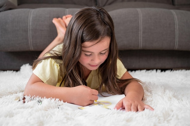 Foto alegre menina deitada no chão desenhando