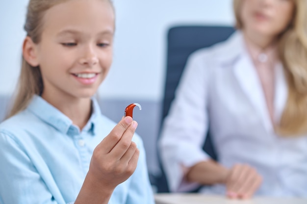 Alegre menina em idade escolar com aparelho de escuta na mão